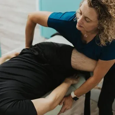 An FST practitioner guiding a client through a supported hip stretch on the treatment table
